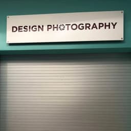 Teal storefront with a white DESIGN PHOTOGRAPHY sign above a closed grey shutter.