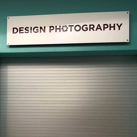 Teal storefront with a white DESIGN PHOTOGRAPHY sign above a closed grey shutter.