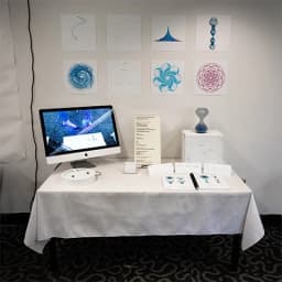 Gallery table with geometric spiral prints, an iMac, and a blue glass spiral sculpture.