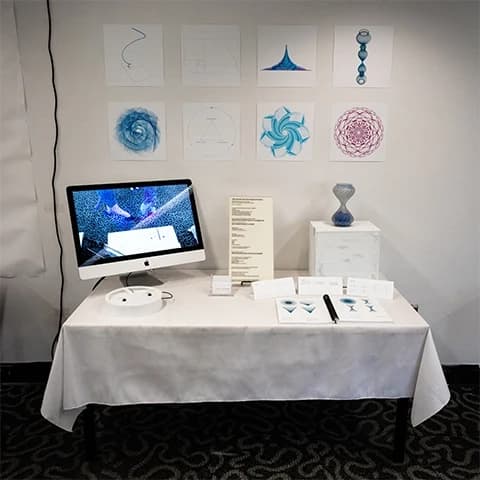 Gallery table with geometric spiral prints, an iMac, and a blue glass spiral sculpture.