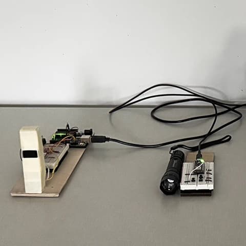 Arduino and breadboard prototype with a white sensor tower, green LED module, and flashlight.